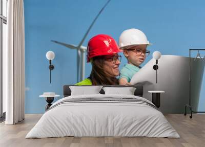 Concept of transfer of experience to the future generation. Woman engineer in red helmet shows her little son in glasses and white helmet work plan of a windmill Wall mural