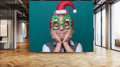 Portrait of happy little boy wearing headband with Santa Claus Hat and funny glasses with Christmas trees Wall mural