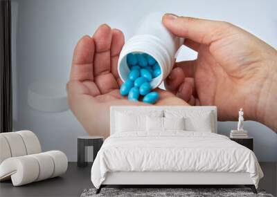 A woman pours blue pills from a plastic jar into her palm. Wall mural