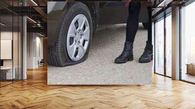 A young woman stands near her car with a flat tire. Wall mural