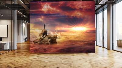 A man with spread arms standing on a rock protruding above the clouds and looking at a flare on the horizon. Wall mural