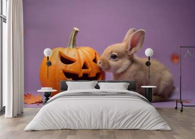 A baby rabbit with soft brown fur next to a large, grinning Halloween pumpkin on a purple background a small tan puppy is curiously sniffing the pumpkin the image includes a few scattered fall leaves Wall mural