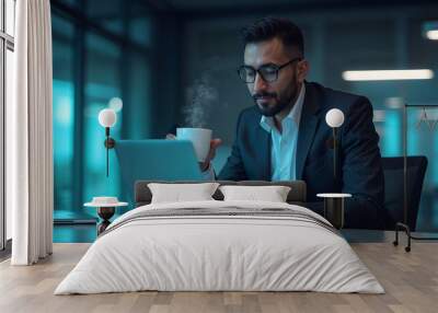 Man entrepreneur in smart casual attire, holding a steaming cup of coffee, using a silver laptop Wall mural