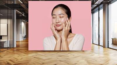 Young Asian beauty woman pulled back hair with korean makeup style touch her face and perfect skin on isolated pink background. Facial treatment, Cosmetology Wall mural