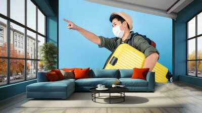 Asian tourists wear a mask. He carried a suitcase and pointed to an empty space on a blue background. Wall mural