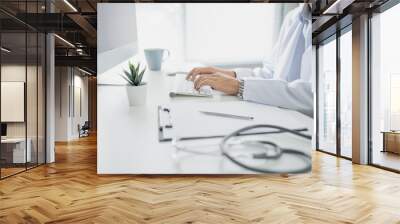 Doctor was sitting and working with the computer on the table in the office. Wall mural