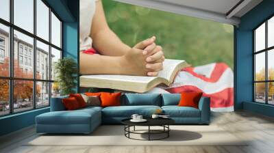 Believe faith and charity, A calm young woman shows gratitude, folded hands in prayer on the open bible, and the American flag and meditates .praying to request God for help. forgiveness concept. Wall mural