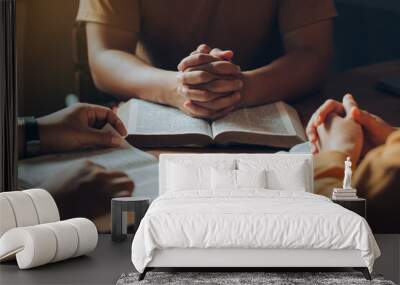 Christians and Bible study concept.Christian family sitting around a wooden table with open bible page and holding each other's hand praying together. Wall mural