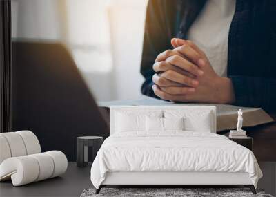 Women's hands are folded in prayer on a Holy Bible over a laptop in church concept for faith, religion, love, and forgiveness. Holy Bible study reading together in Sunday school.Online church Wall mural