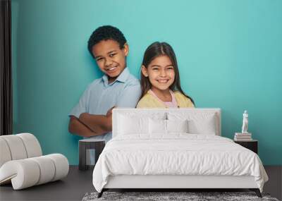 Asian girl and African American boy standing back to back with arms crossed on a turquoise background Wall mural