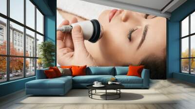 Brunette woman receiving radiofrequency lifting procedure for her face skin rejuvenation at aesthetic cosmetology clinic Wall mural