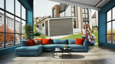 Family sitting on lawn in backyard, big modern house on background Wall mural