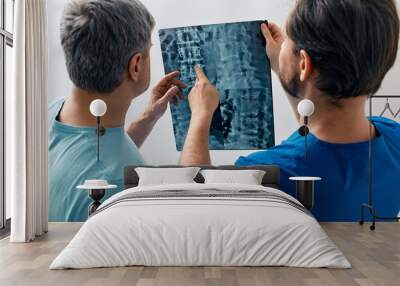 Manual therapist viewing X-ray of backbone with his male patient with spinal problem during medical consultation at hospital Wall mural