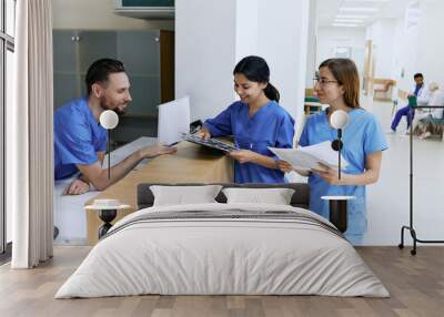 Medical employees. Medical assistant on duty talking with female nurses while working day in hospital standing near reception desk at lobby Wall mural