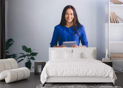 young woman holding digital tablet, smiling and looking at camera while standing at modern office. Wall mural