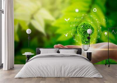 Hand holding light bulb against nature on green leaf with icons energy sources for renewable, sustainable development. Technology ,Environment ,Ecology concept. Wall mural