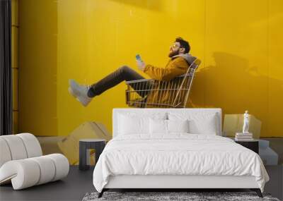 man sitting in shopping trolley and box on yellow background Wall mural