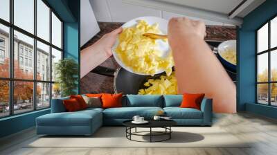 Hands throwing laminated potatoes from a white plate to black pan. Spanish omelet recipe. Wall mural