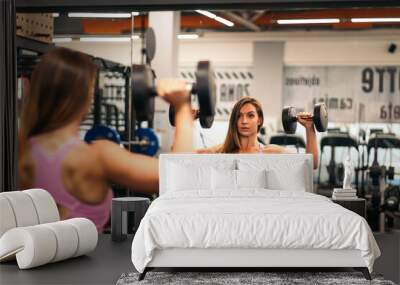 woman athlete training with dumbbells in front of the mirror in a gym Wall mural