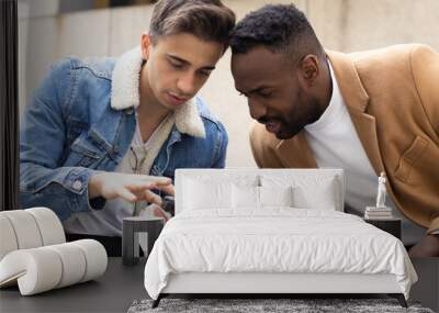 Young man showing his friend something on the mobile while they are sitting Wall mural