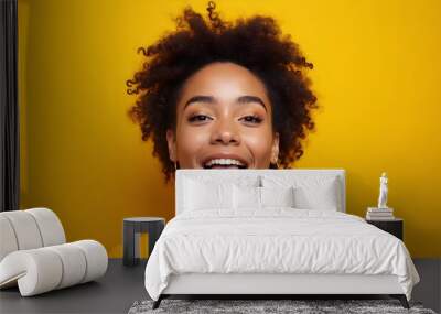 Happy young woman with afro hair sticking out her tongue against yellow background. Wall mural