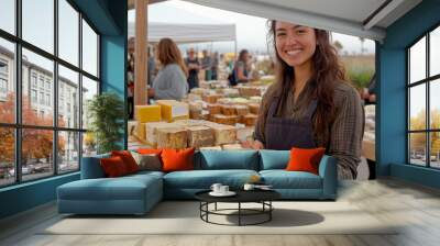 A cheerful woman wearing an apron smiles while holding a handcrafted bar of soap at an outdoor market. Wall mural