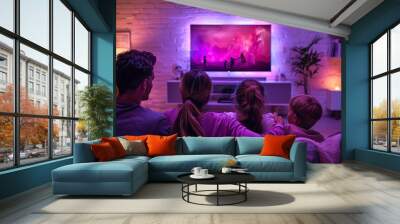 A family of four, two adults and two children, enjoy a movie night together in a warmly lit living room. The room is bathed in ambient purple and pink lighting from the television screen. Wall mural