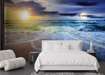 day and night time change concept above sea tide on a cloudy twilight. green waves crashing golden sandy beach with sun and moon above the horizon. storm weather approaching. summer holiday concept Wall mural