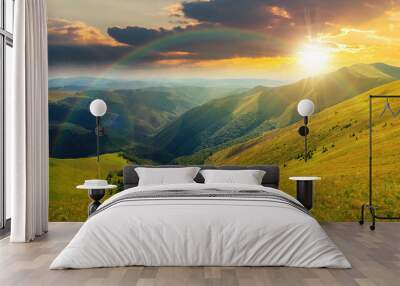 mountain landscape in summer at sunset. grassy meadows on the hills rolling in to the distant peak beneath a rainbow in evening light Wall mural