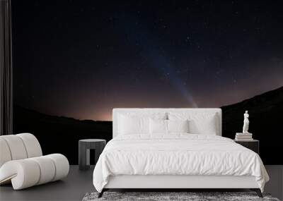 Adventurous man watching the stars on a beach at night with his headlamp shinning up at the stars. Wall mural