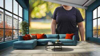 Young plus size woman wearing blank empty black tshirt mockup for design template in the park Wall mural