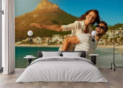 Portrait, couple and piggyback by ocean for love, commitment and bonding on summer vacation for honeymoon. Man, woman and freedom on beach for romantic holiday, airplane and weekend with energy. Wall mural