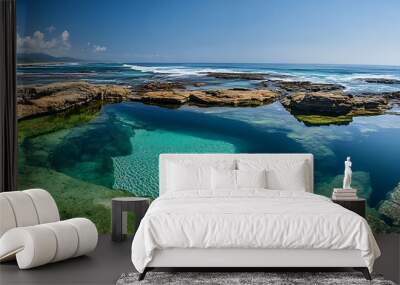 A natural rock pool filled with crystal clear water, surrounded by a rocky coastline and the ocean beyond. Wall mural