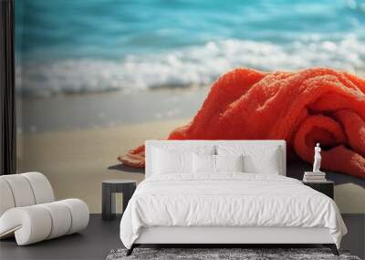 Orange towel on a white sandy beach with waves in the background. Wall mural