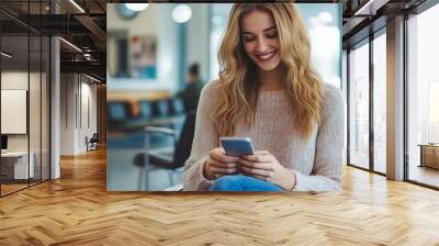 Smiling young woman using phone while waiting in a lobby. Wall mural