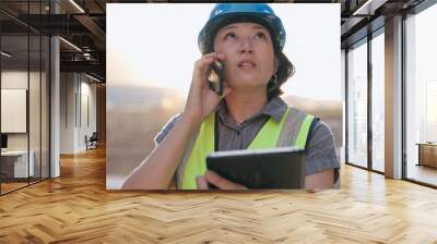 Asian woman, phone call and tablet, construction worker and inspection of building site for project management. Architecture, engineer and communication, contractor and affirmative action outdoor Wall mural