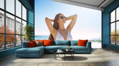 Beach, relax and happy woman with bikini for holiday, summer vacation or travel outdoor. Stretching, smile and girl at sea with swimsuit, sunglasses or body pose for cool fashion on tropical island Wall mural