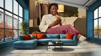 Black girl, happy and smartphone on sofa in home scrolling or online social media memes, videos and funny text. Woman, texting and mobile on couch to relax with entertainment, streaming and internet. Wall mural