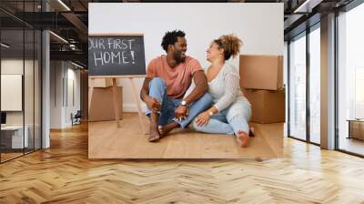 Board, box or happy couple laughing in new house in real estate, property investment or buying apartment. Our first home, words or man on floor with smile, sign or woman to celebrate moving in rent Wall mural