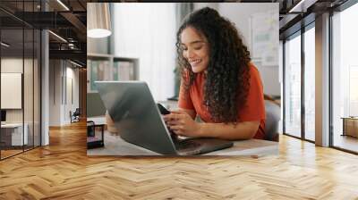 Business woman, laptop and smile for phone, communication and networking for startup in office. Happy, female employee event planner checking email on computer, social media and post on smartphone Wall mural