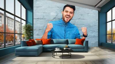 Celebration, portrait and man by brick wall with success for achievement, energy and winning lottery. Excited, wow and male winner in city with positive feedback for promotion and exclusive discount Wall mural