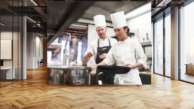 Chef, teamwork and kitchen or pan cooking for hospitality service as preparation, learning or catering. Man, woman and hat at stove for teaching skill for fine dining presentation, recipe or cuisine Wall mural