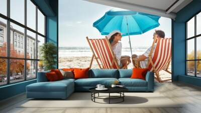 Couple, relax and beach chairs with umbrella on sand for vacation, holiday or weekend break. Summer, man and woman together in nature with water for peace, travel or tourism in Bali getaway with view Wall mural