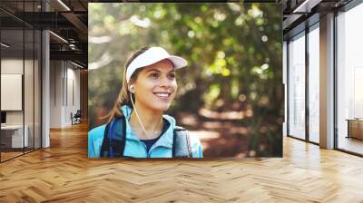 Earphones, thinking and happy woman hiking in nature on outdoor adventure to explore on holiday vacation. Sightseeing, relax and hiker trekking in woods for training or travel for streaming music Wall mural