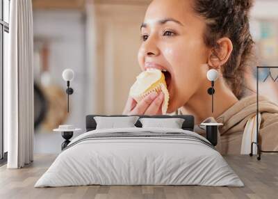 Eating, cupcake and woman in home for dessert, sweet treat or sugar snack in kitchen. Bite, tasting and female person with vanilla cake for cheat meal, hungry and enjoy delicious food in apartment Wall mural