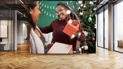 Female people, happy and gift with Christmas tree for festive, holiday and celebration as friends in home. Women, together and love with presents, excited and solidarity for relationship in December Wall mural