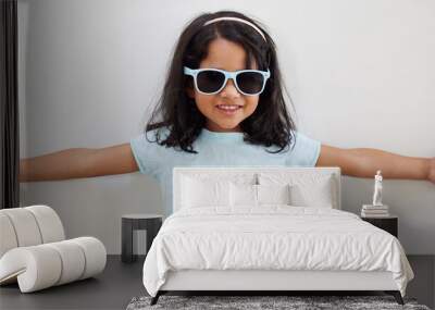 Girl, child and smile with sunglasses by wall for summer, holiday and playful at family home. Kid, excited and happy with eyewear, games and fashion with trendy style, growth and development at house Wall mural