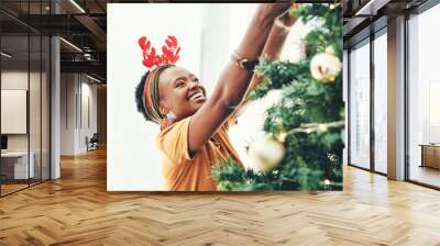 Happy, black woman and tree with decor for christmas, festive celebration or new year at home. Young African, female person and smile in joy with reindeer antlers or decorations for December holiday Wall mural