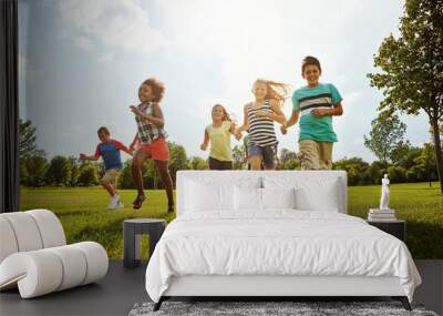 Happy kids, diversity and running with friends in nature for fun, playful day or summer at park. Group of excited children or youth enjoying sunny outdoor holiday or weekend on grass field together Wall mural