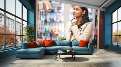 Happy woman, thinking and grocery shopping with basket for choice on ingredients, food or stock at supermarket. Female person, consumer or shopper with smile or cart in wonder or decision at store Wall mural